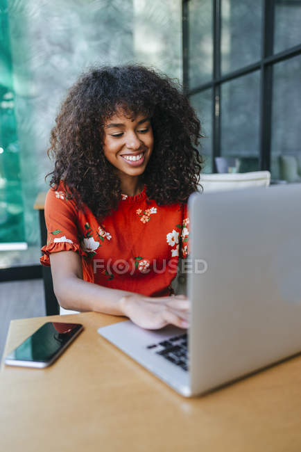 Portrait of smiling young woman  using laptop in a coffee shop — Stock Photo