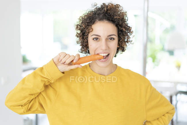 Portrait de femme mangeant une carotte à la maison — Photo de stock