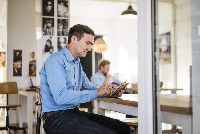 Бизнесмен сидит за столом с планшетом — стоковое фото