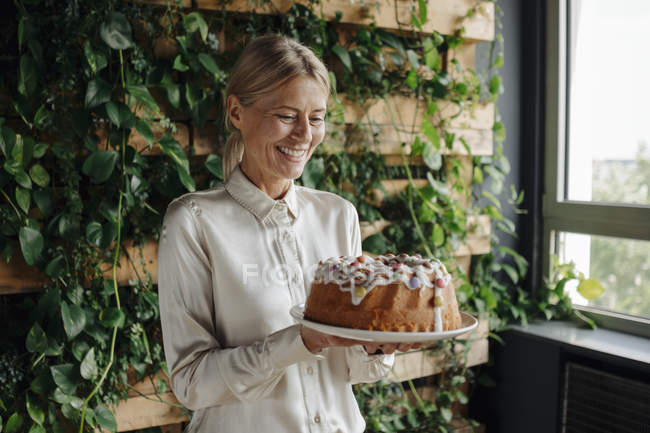  Mujer de negocios sonriente sosteniendo pastel de cumpleaños en la oficina verde — Caucásica, Medio ambiente