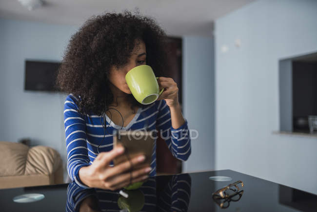 Молода жінка п'є каву, дивлячись на мобільний телефон. — стокове фото