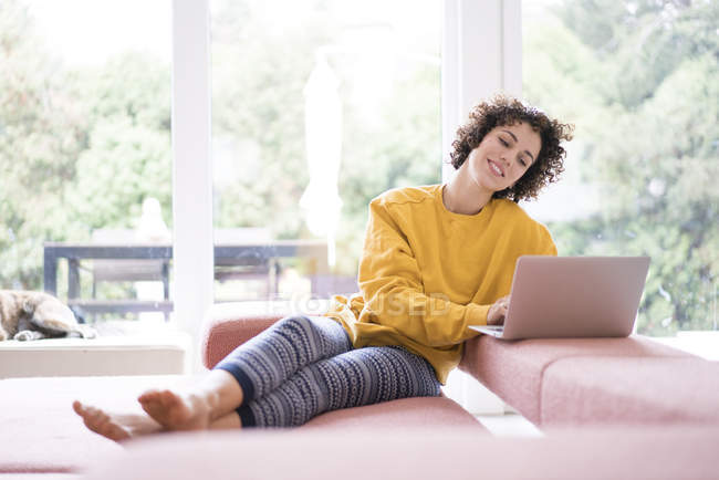 Smiling woman using laptop on couch at home — Stock Photo