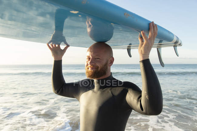 Espanha, Andaluzia, Tarifa, retrato de homem sorridente carregando stand up paddle board no mar — Fotografia de Stock