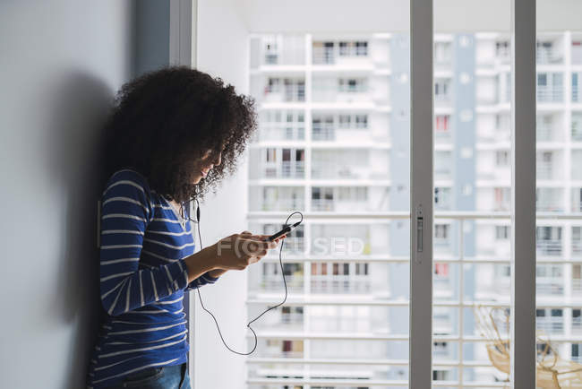 Mujer joven usando teléfonos inteligentes y auriculares en casa - foto de stock