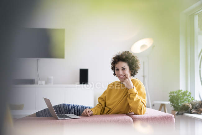 Femme souriante utilisant un ordinateur portable sur le canapé à la maison — Photo de stock