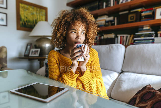 Young woman with curly hair holding mug at home — Stock Photo