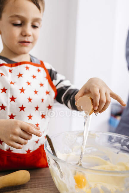 Boy throwing an egg into glass bowl for preparing dough — Stock Photo