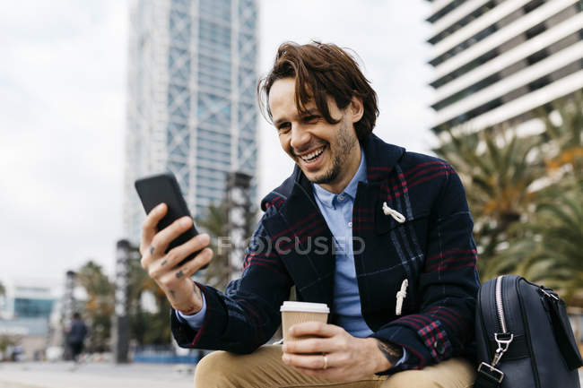 Іспанія, Барселона, щасливий чоловік, що сидить у місті з кавою та мобільним телефоном. — стокове фото