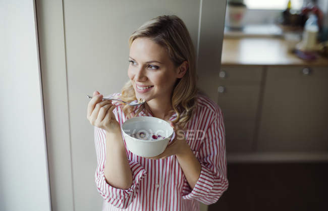 Mujer sonriente desayunando en casa por la mañana - foto de stock