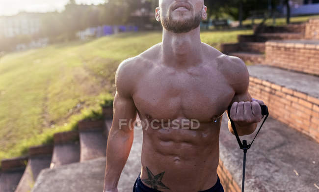 Sección media del hombre musculoso barechested que ejerce con el expansor al aire libre - foto de stock