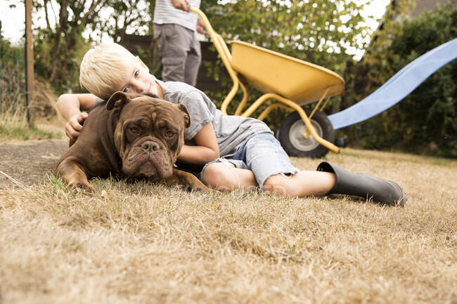 Boy cuddling with Old English Bulldog at playground in garden. - foto de stock