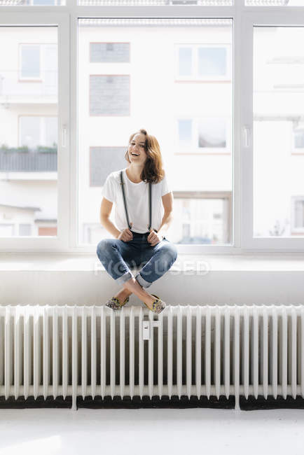 Mujer riendo sentada en el alféizar de la ventana - foto de stock