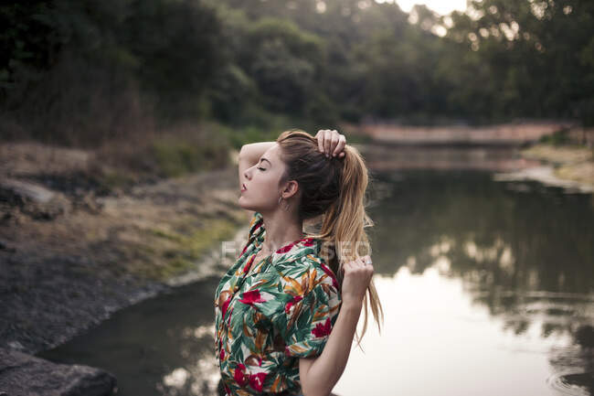 Jovem mulher tocando seu cabelo ao lado de um lago — Fotografia de Stock