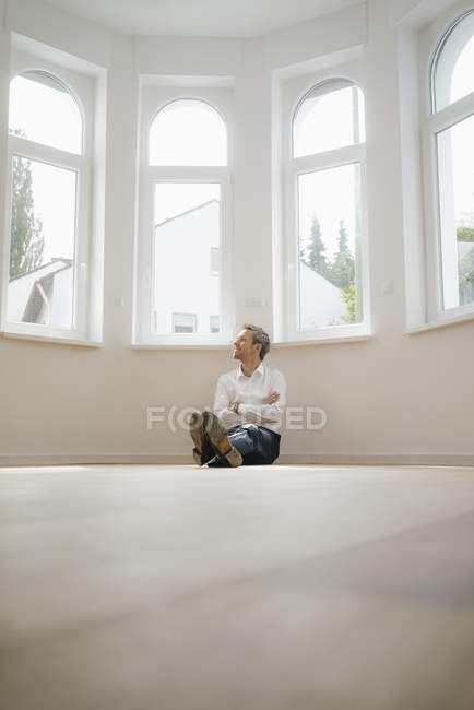 Uomo d'affari seduto a terra della sua casa appena ristrutturata, cercando felice — Foto stock