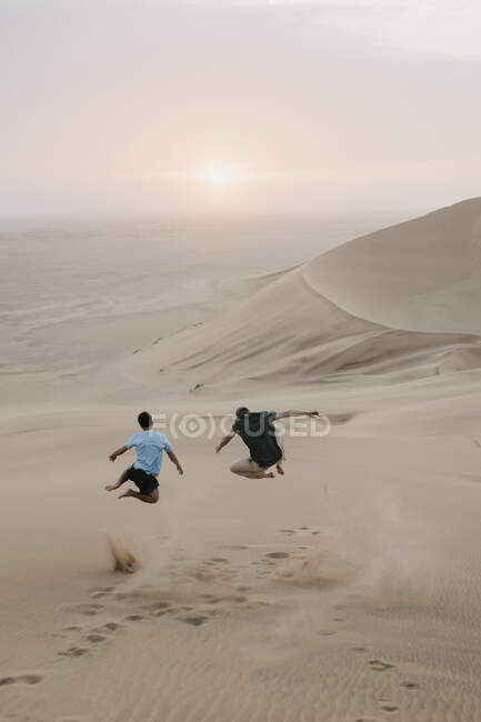 Namibia, Namib, vista posteriore di due amici che saltano nell'aria sulla duna del deserto — Foto stock