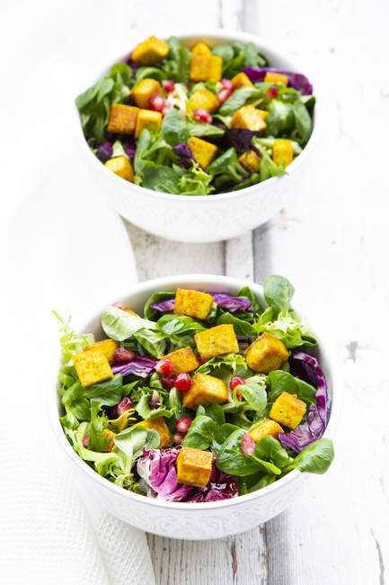 Mixed salad with roasted tofu, red cabbage, pomegranate seeds and curcuma in bowl on white wood — Stock Photo