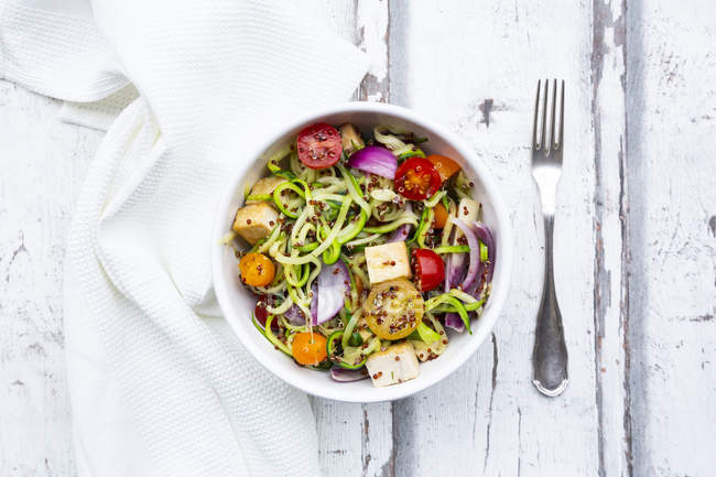 Bowl of zoodles with fried tofu, red quinoa, red onions and tomatoes — Stock Photo