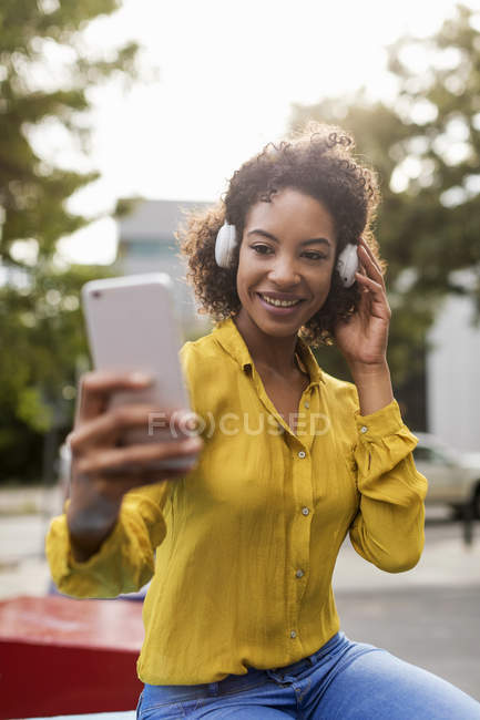 Retrato de mujer sonriente escuchando música con auriculares tomando selfie con smartphone - foto de stock