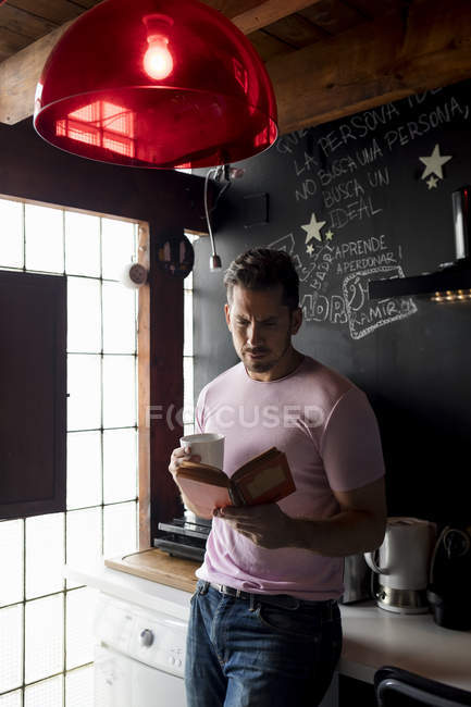 Man with cup of coffee reading a book in kitchen — Stock Photo