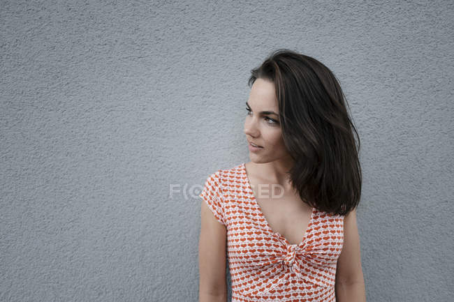 Retrato de uma mulher bonita, de pé na frente da parede, olhando para longe — Fotografia de Stock