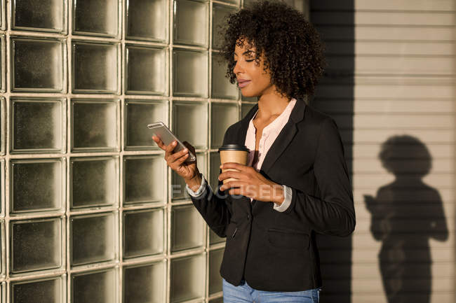 Businesswoman with coffee to go looking at cell phone at evening twilight — Stock Photo
