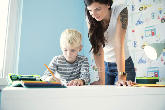 Mutter hilft Sohn bei Hausaufgaben am Schreibtisch — Stockfoto