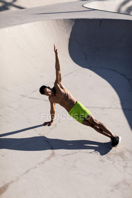 Barechested homem muscular fazendo pranchas laterais em um parque de skate — Fotografia de Stock