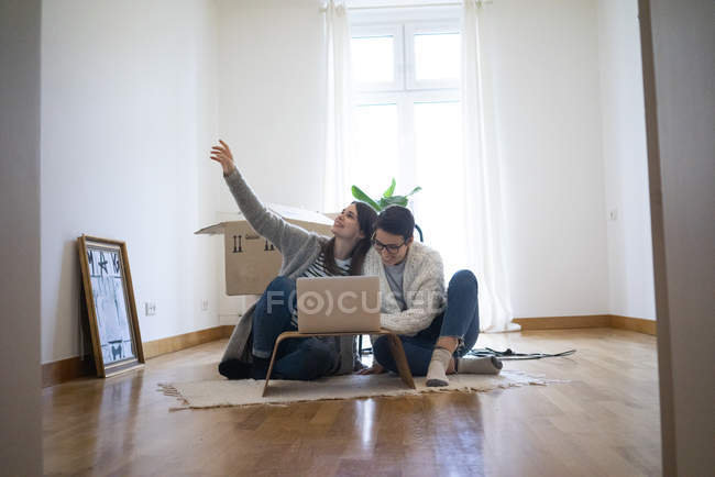 Junge Frauen, die auf dem Boden ihres neuen Hauses sitzen und Laptop benutzen — Stockfoto