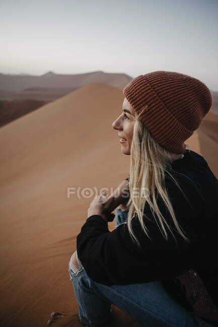 Namibia, Namib desert, Namib-Naukluft National Park, Sossusvlei, smiling woman sitting on Dune 45 at sunrise — Stock Photo