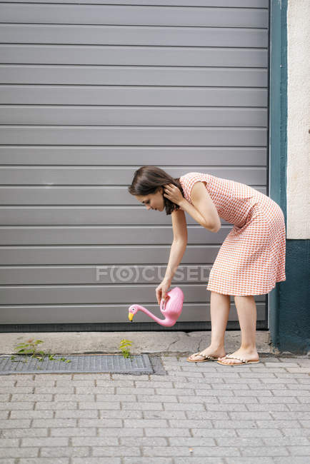 Woman watering plants with a flamingo can in an urban street — Stock Photo