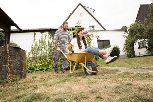 Giocoso uomo spingendo donna seduta in carriola in giardino — Foto stock