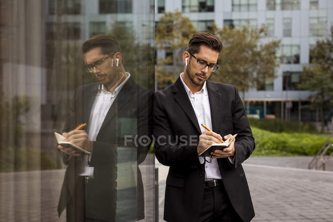 Бізнесмен з навушниками в місті, які пишуть у щоденник — стокове фото