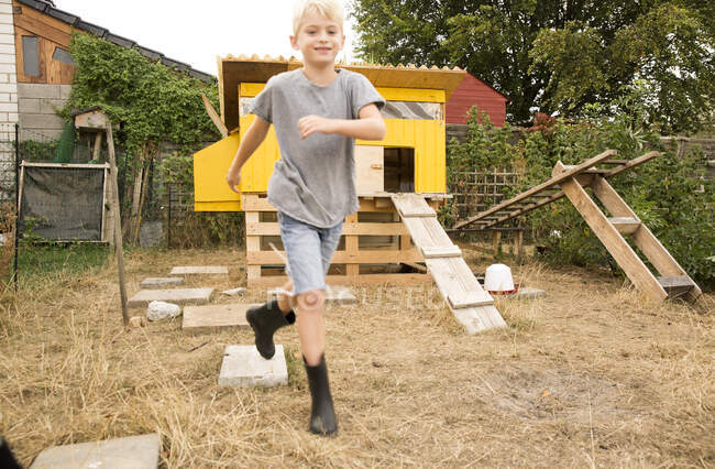 Portrait of happy boy running at chickenhouse in garden — Stock Photo