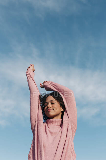 Portrait d'une jeune femme souriante vêtue d'un pull-over rose contre le ciel — Photo de stock