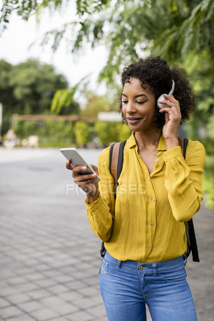 Femme souriante écoutant de la musique avec écouteurs et smartphone à l'extérieur — Photo de stock