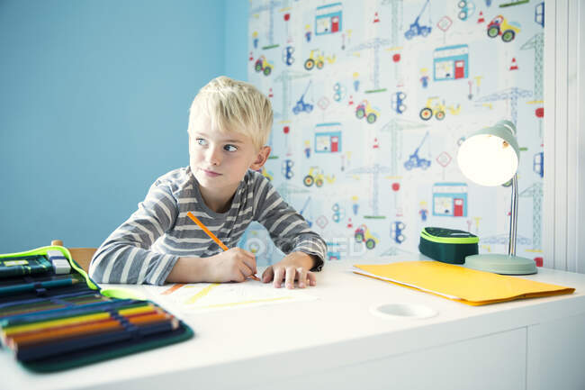 Мальчик выполняет домашнюю работу за партой в детской комнате — стоковое фото