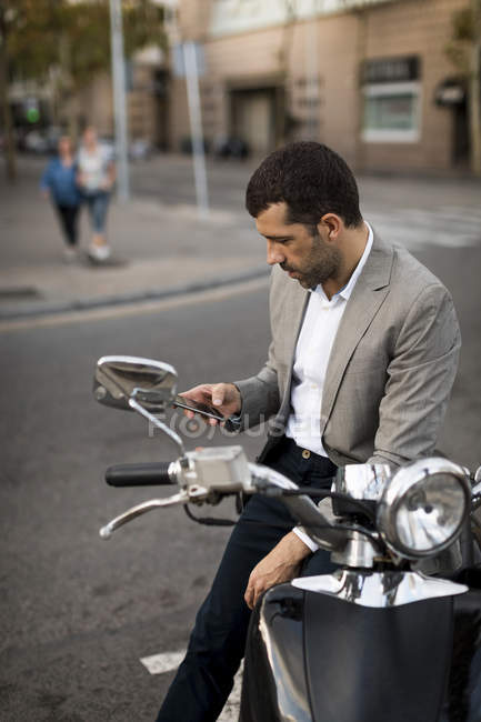 Empresario en moto comprobando el teléfono celular - foto de stock