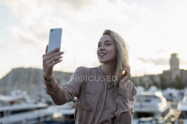 Улыбающаяся молодая женщина делает селфи на набережной — стоковое фото
