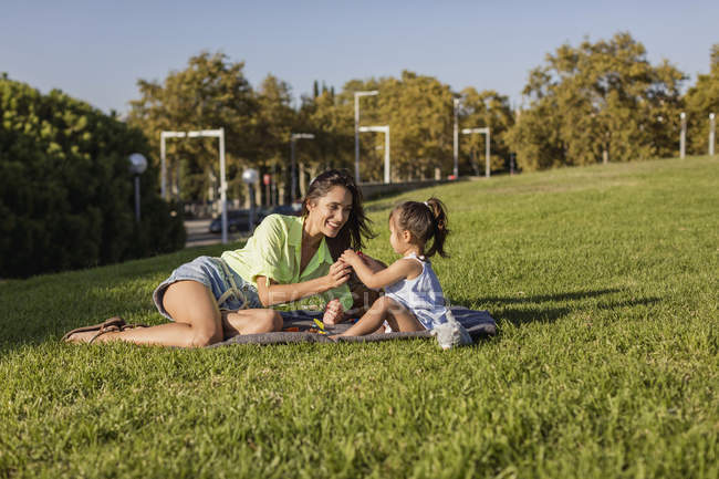Felice madre che gioca con la figlia su una coperta nel parco — Foto stock