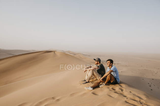 Namibie, Namib, deux amis assis sur une dune désertique regardant — Photo de stock