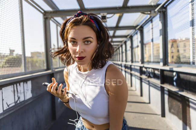 Retrato de mulher jovem com fones de ouvido e telefone celular em uma ponte — Fotografia de Stock