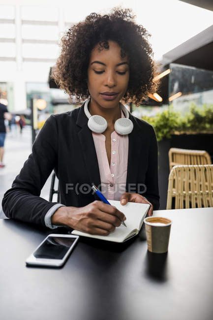 Retrato de una mujer de negocios tomando notas en la cafetería del pavimento - foto de stock