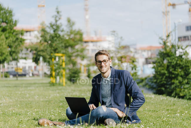 Junger Geschäftsmann sitzt im Park und benutzt Laptop — Stockfoto