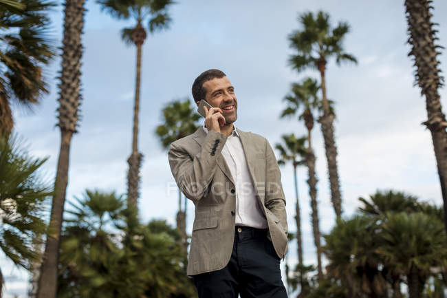 Happy businessman talking on cell phone with  palm trees in background — Stock Photo
