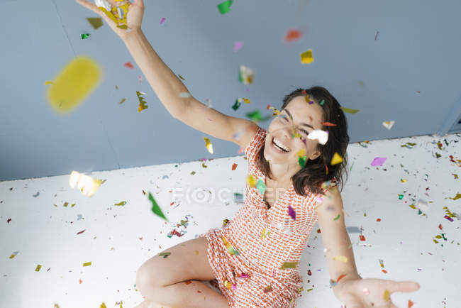 Mujer feliz sentada en el suelo, lanzando confeti - foto de stock