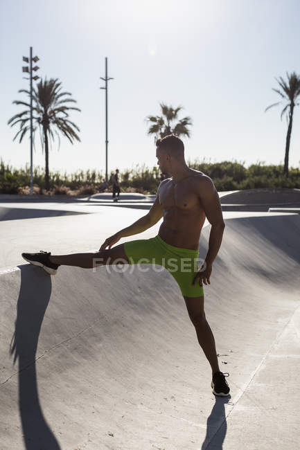Barechested homem muscular fazendo exercício de alongamento em um parque de skate — Fotografia de Stock
