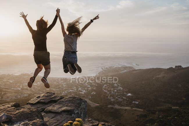 Південна Африка, Кейптаун, Клоф Нек, дві жінки стрибають на скелю під час заходу сонця. — стокове фото