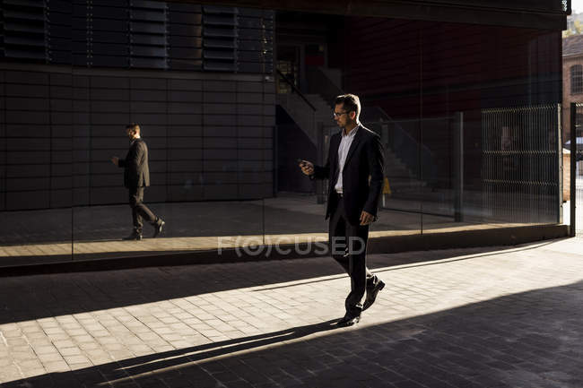 Бизнесмен, гуляющий по городу, проверяет мобильный телефон — стоковое фото