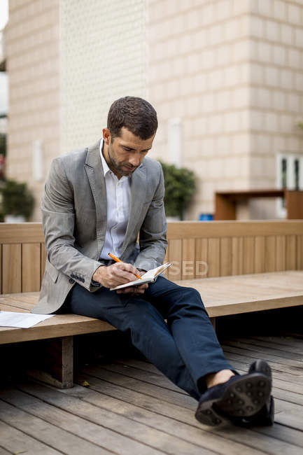 Empresario sentado en un banco escribiendo en el diario - foto de stock