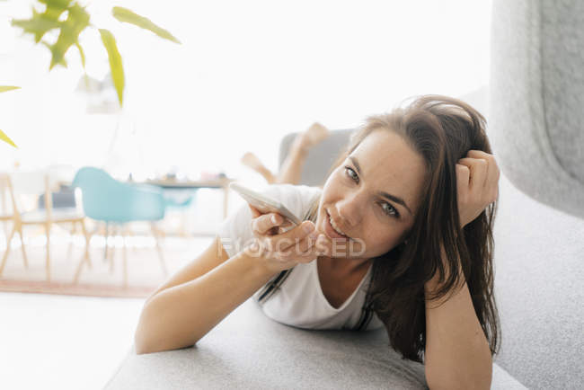 Bella donna seduta sul divano, utilizzando smartphone — Foto stock